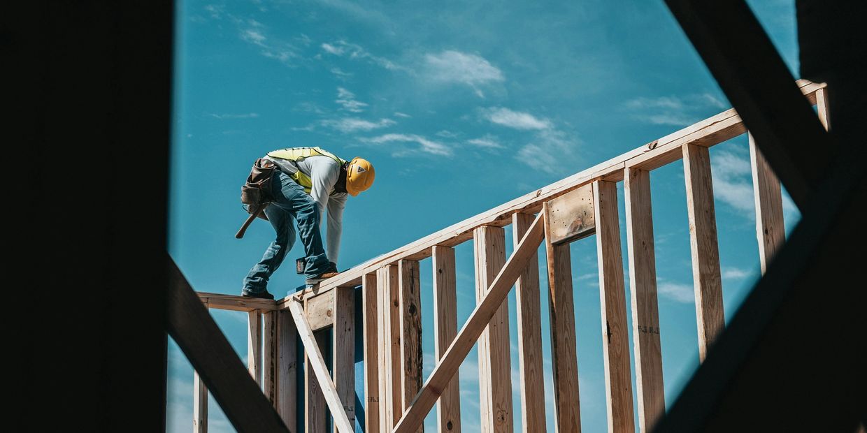 Construction worker on wooden frame under blue sky.