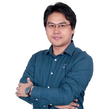 Man in glasses with arms crossed, wearing a blue shirt, posing confidently.