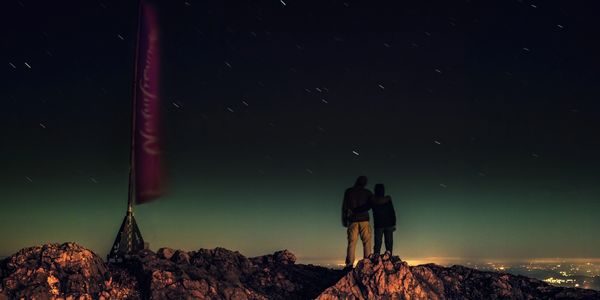 Image of two people holding each other  on a mountain top during a moment in time while the universe