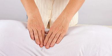 Hands performing a massage on a person covered with a white towel.