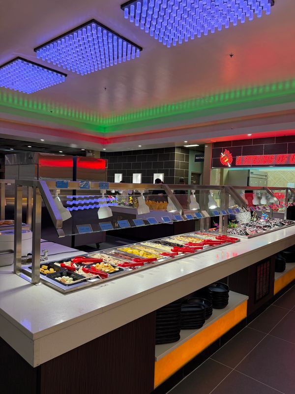 Buffet station with food trays, sneeze guards, and colorful ceiling lights