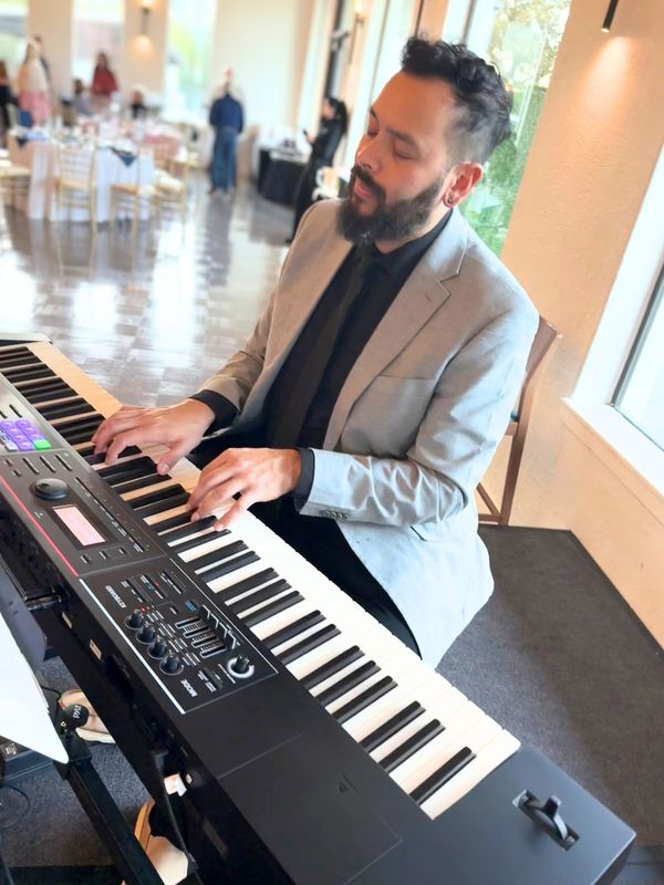 Man in a gray suit playing a keyboard indoors.