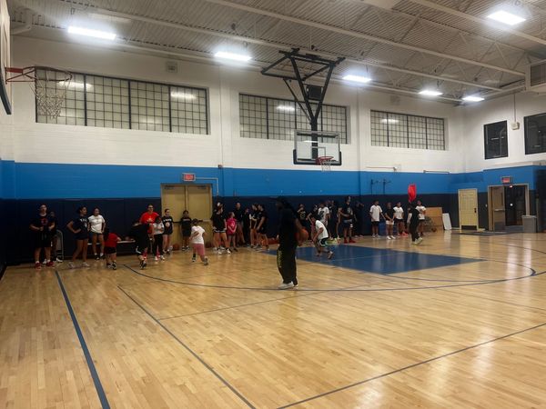 Group of people gathered inside a basketball gymnasium with hardwood floors.
