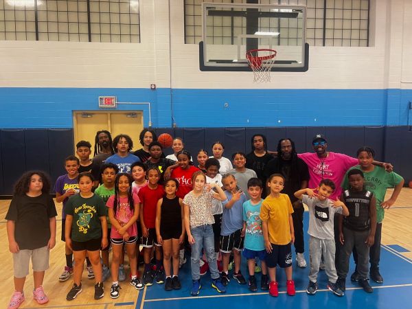 Group of children and adults posing inside a gym basketball court.