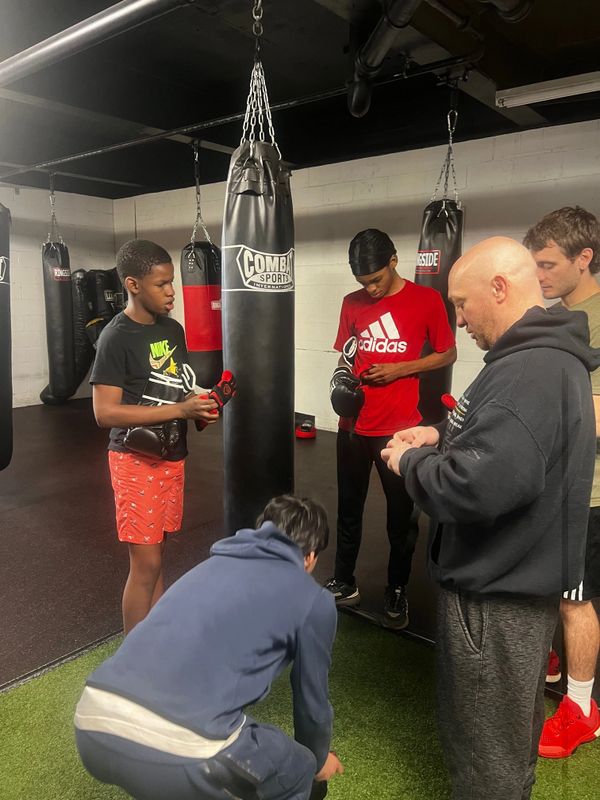Five people in a gym preparing boxing gloves near punching bags.