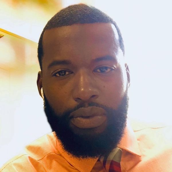 Close-up portrait of a bearded man in an orange shirt and tie.