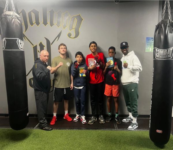 Group of six people posing with boxing gloves and books in a gym.