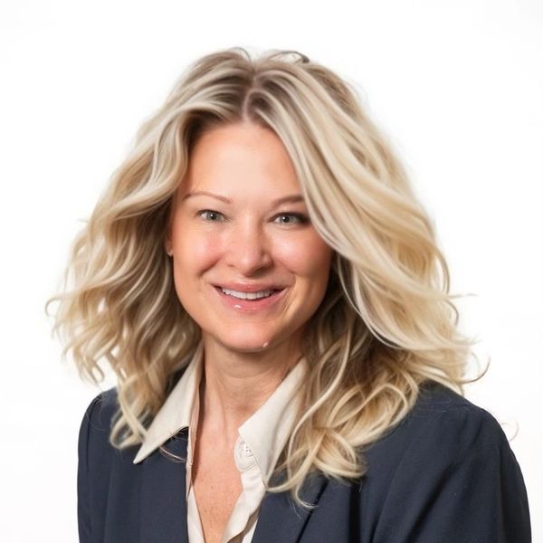 Smiling woman with wavy blonde hair in professional attire against a white background.