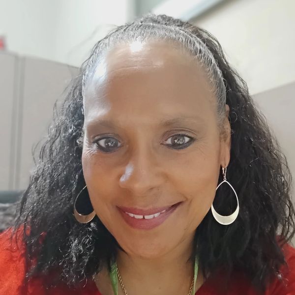 Smiling woman with curly hair wearing large hoop earrings and a red top.