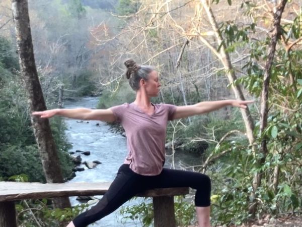 Betsy Jane Butner in yoga pose on park bench overlooking river in Cherokee, NC.