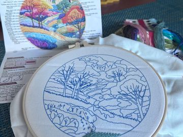 Embroidery hoop with landscape pattern and colorful thread guide.