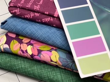 Stack of colorful patterned fabrics with a color swatch card on a cutting mat.