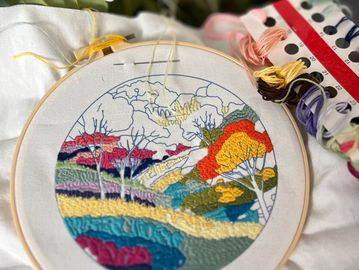 Colorful embroidery of a scenic landscape in progress with threads and floral background.