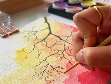 Hand painting delicate tree branches with watercolors on textured paper.