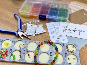 Jewelry-making tools and colorful beads arranged neatly on a wooden table.