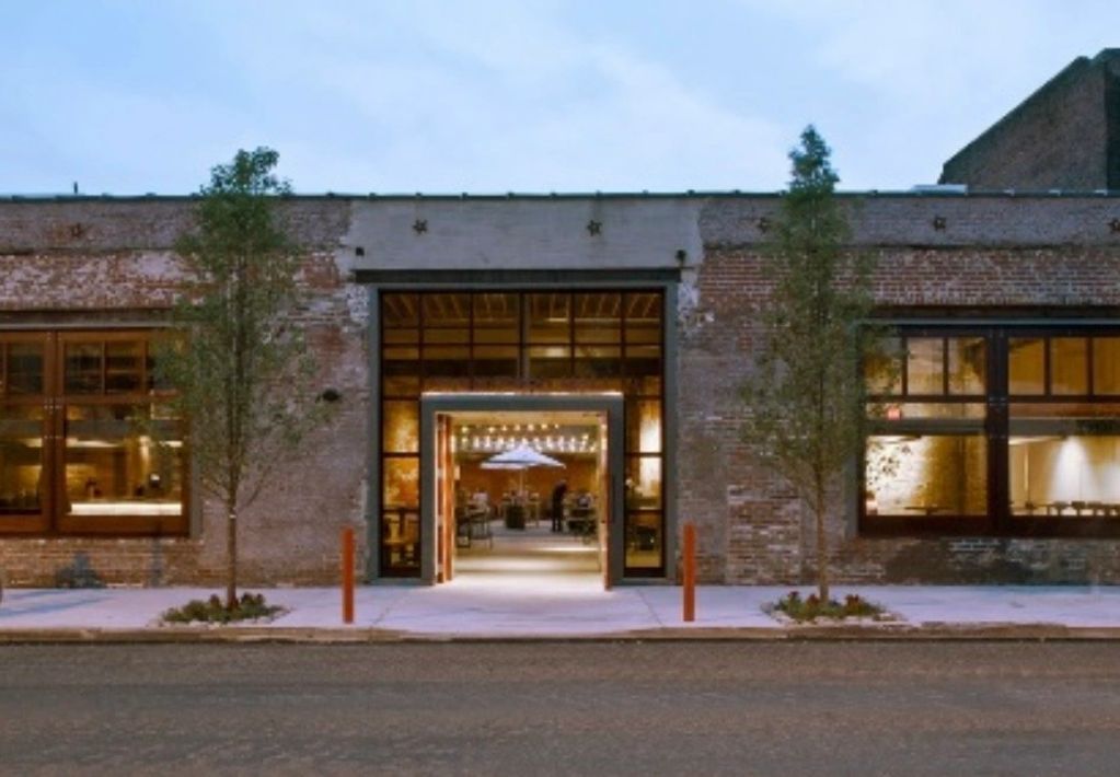 Entrance of a rustic brick building with large windows and warm interior lighting.