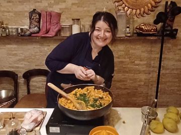 Woman cooking a dish in a kitchen, smiling at the camera.