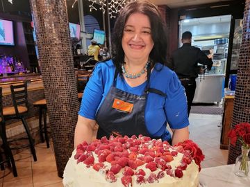 Woman smiling behind a large cake topped with raspberries.