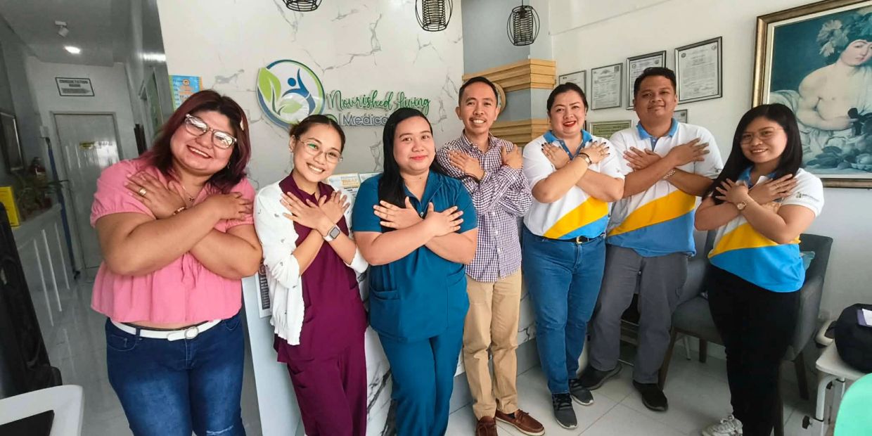 A group of seven people smiling with arms crossed over their chests inside a medical office.