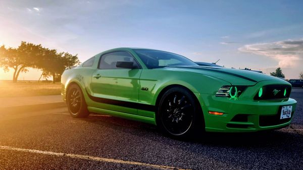 Bright green Ford Mustang with glowing headlights parked at sunset.
