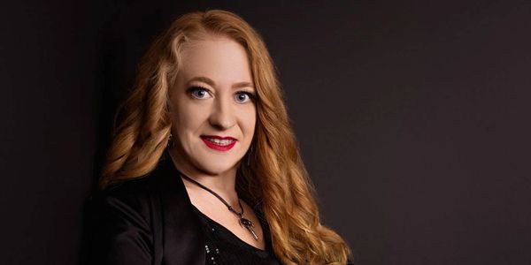 Smiling woman with long red hair and black outfit.