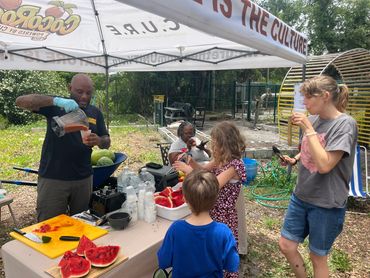 Man serving watermelon to children outdoors.
