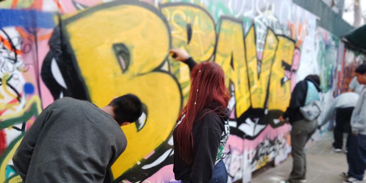 People creating colorful graffiti art on a wall outdoors.