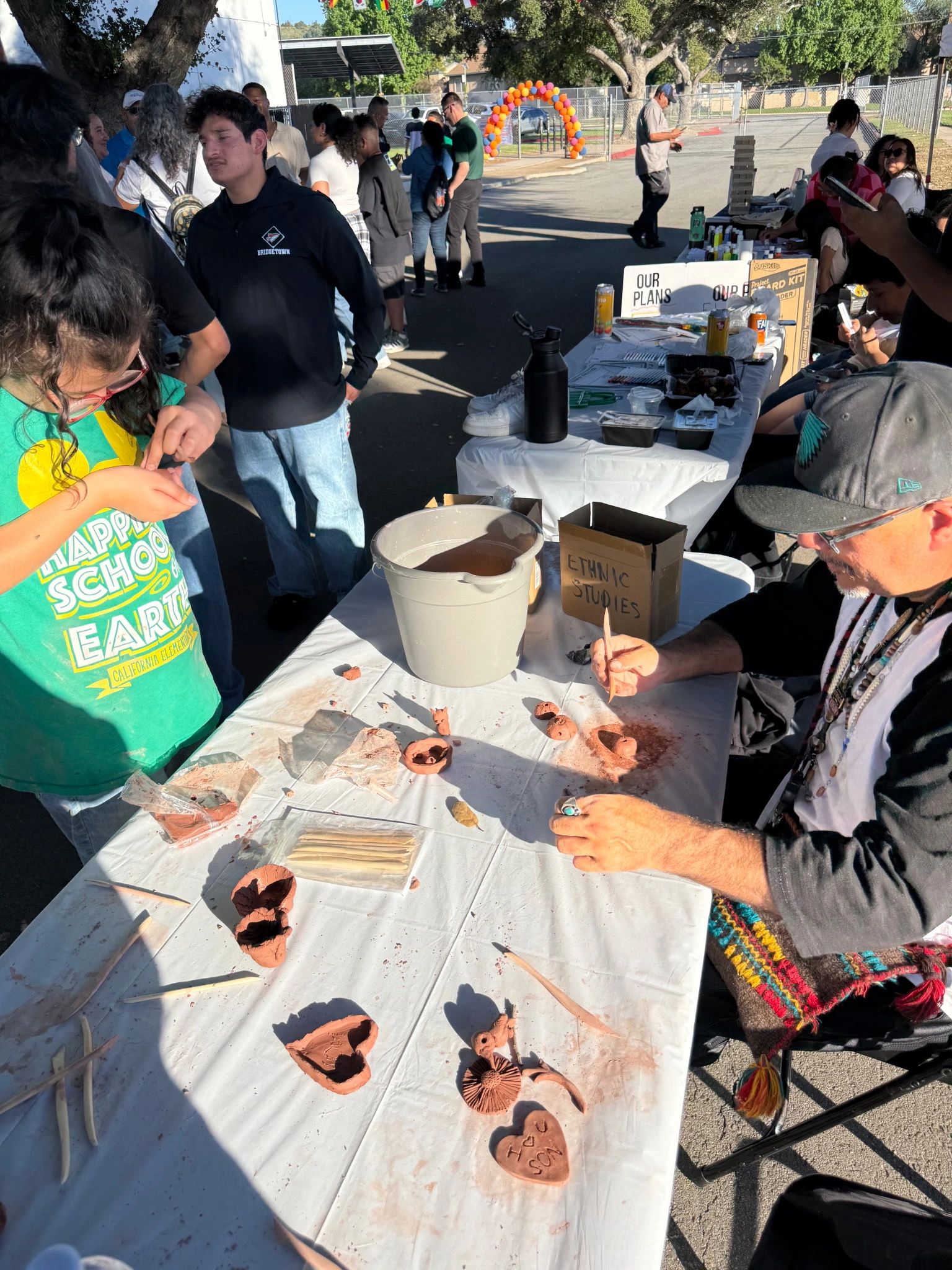 Outdoor ethnic studies craft activity with people shaping clay at a community event.