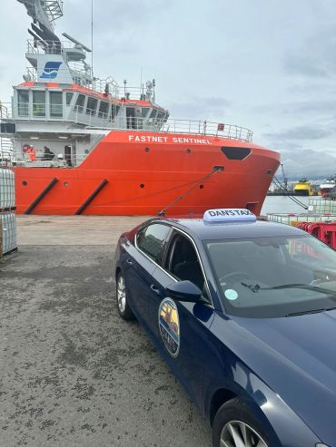 Blue taxi car parked near a large red ship named Fastnet Sentinel.