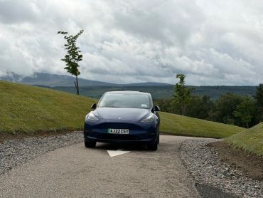 Blue car on a winding road under a cloudy sky.