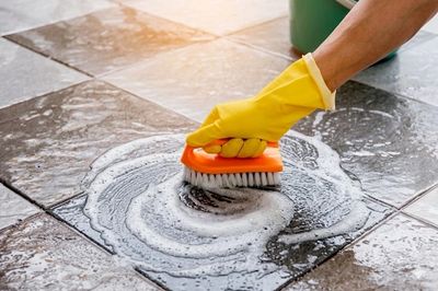 Hand scrubbing tile floor with brush and soap.