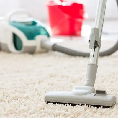 Vacuum cleaner cleaning a beige carpet with a red bucket in the background.