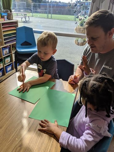 A man helping two children trace their hand