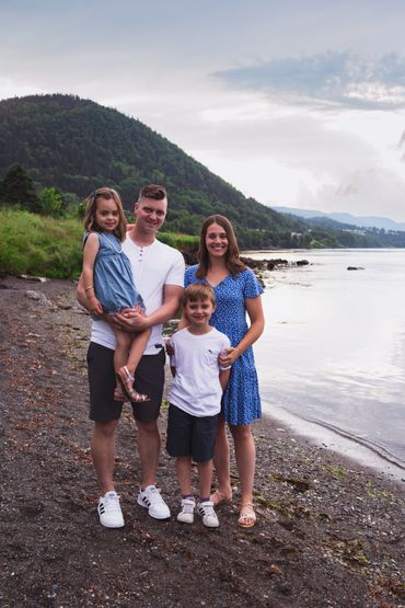 Family of four smiles and poses for camera on beach. 