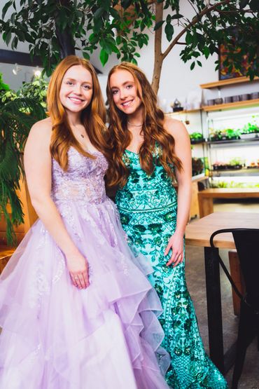 Two women with red hair smile at the camera in purple and green dresses. 