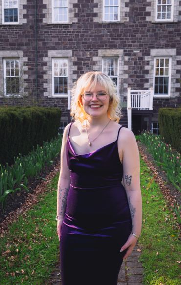 Woman in purple dress smiles in front of brick building. 