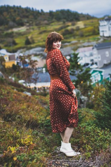 Woman in red dress smiles at camera on grassy hill. 