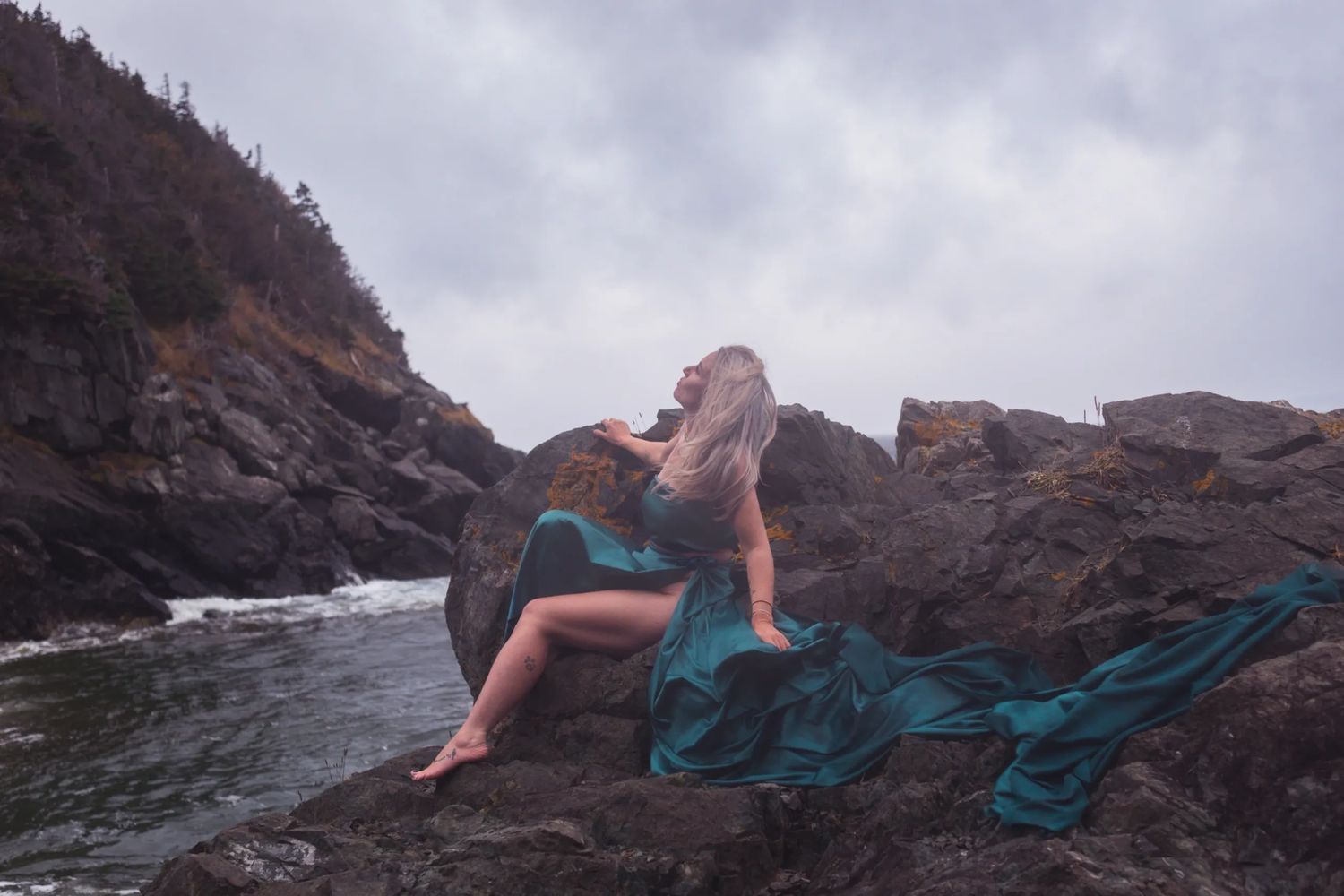 A woman in green silky material poses on a rocky landscape