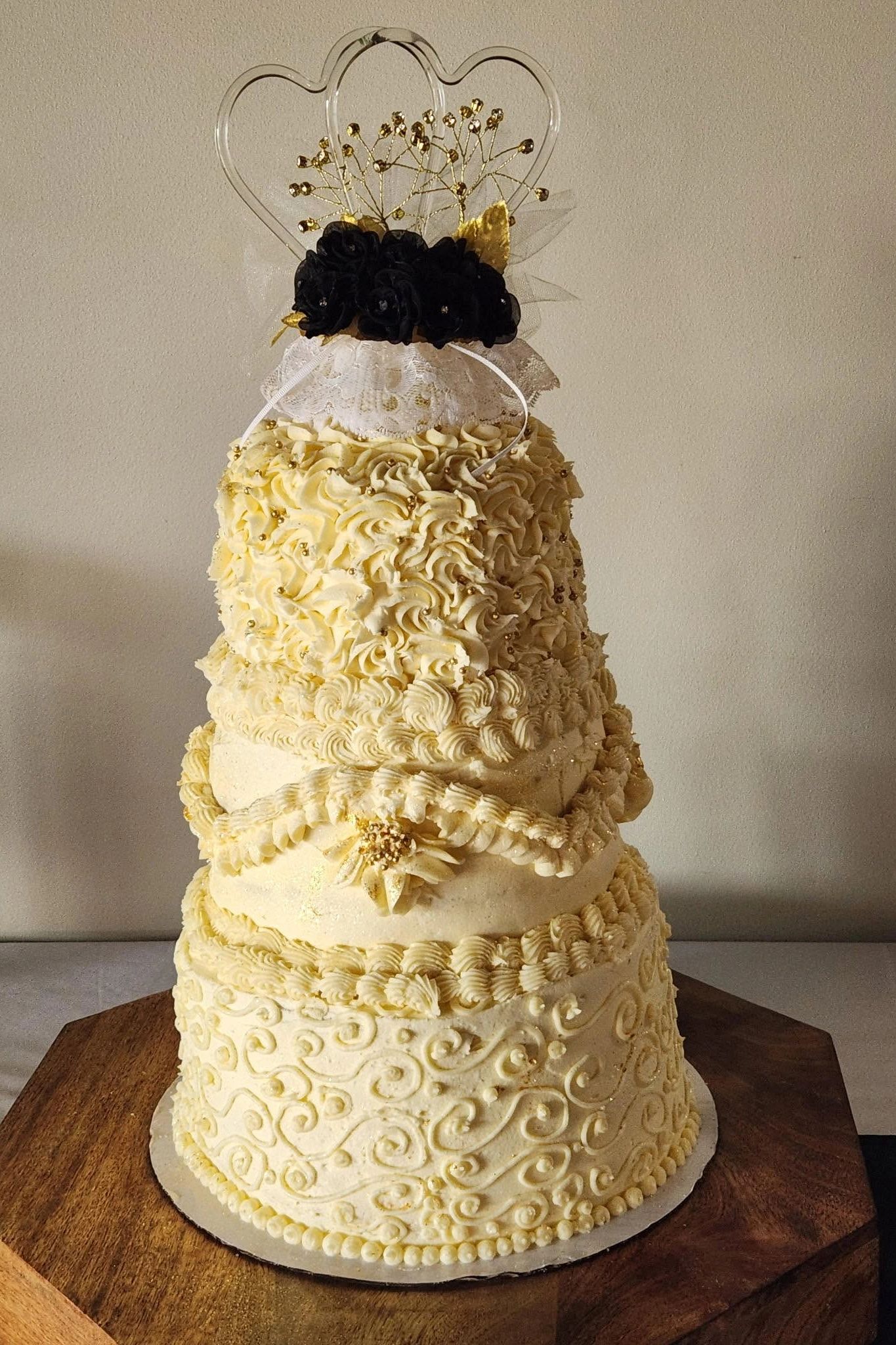 Three-tiered ornate cream-colored cake with black floral topper and gold accents.