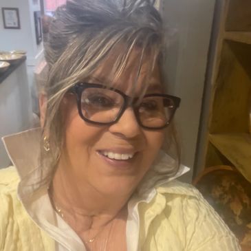 Smiling woman with glasses and light-colored shirt indoors.