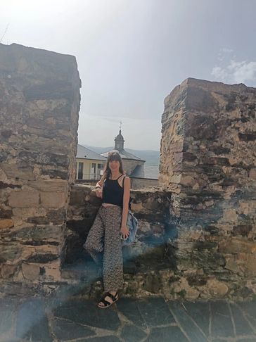 Mujer posando junto a una antigua muralla de piedra.