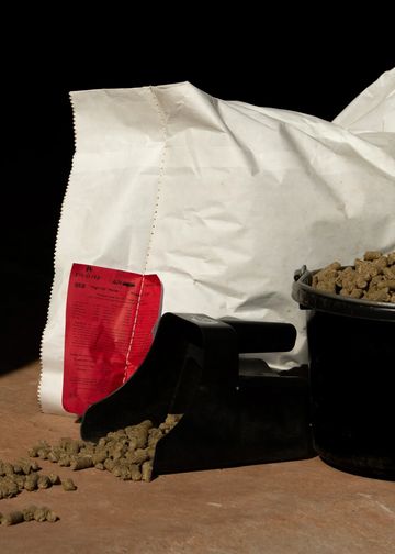 Pellets spilling from a black scoop in front of a white bag and a black bucket.