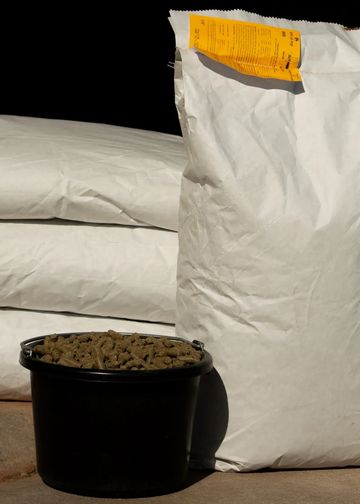A black bucket filled with pellets and large white bags in the background.