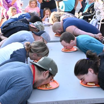 People participating in a pie-eating contest at an outdoor event.