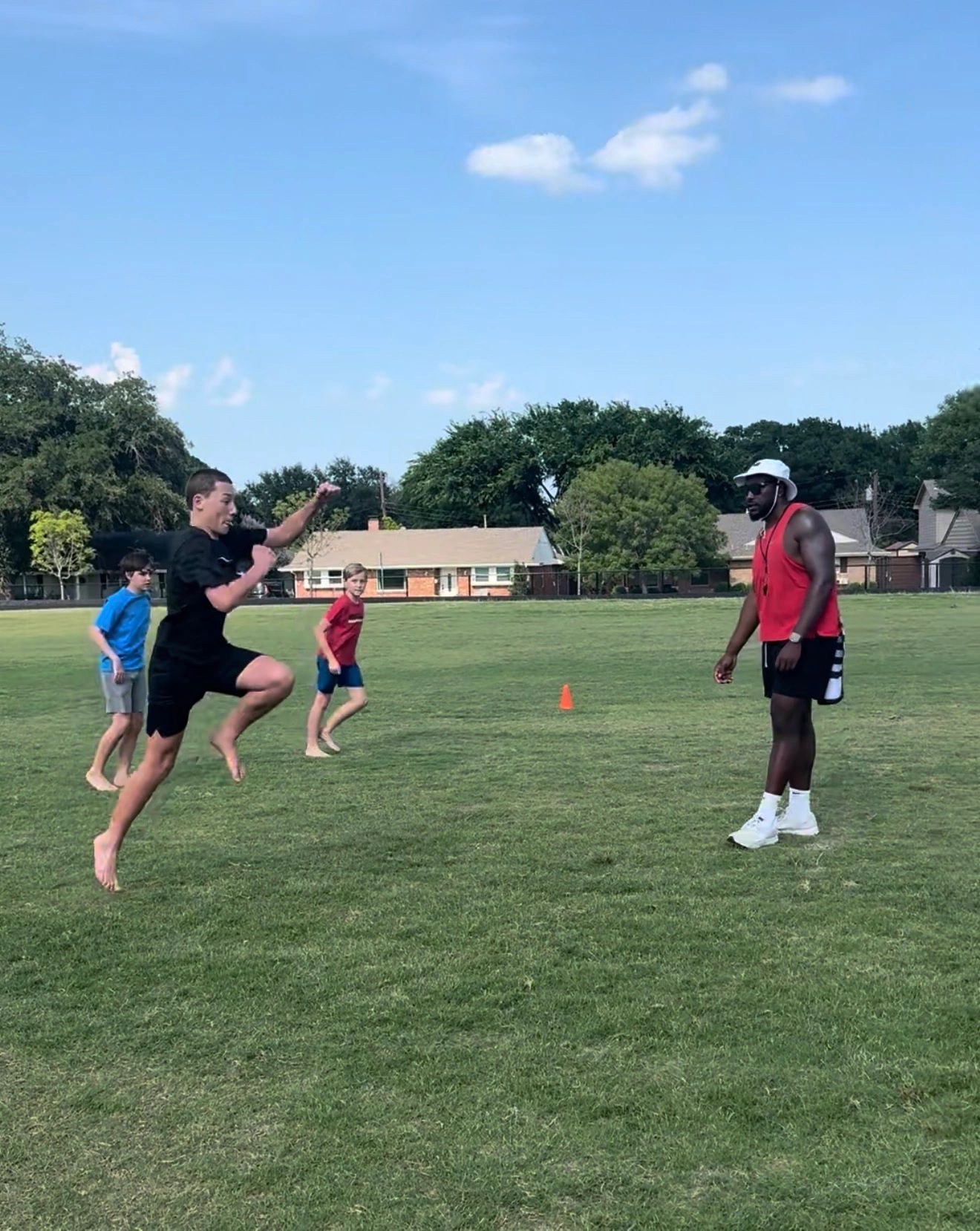 Kids and coach training barefoot on a sunny field with clear skies.