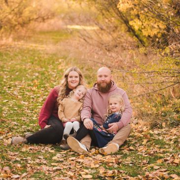 Family of four sitting on a leaf-covered path during autumn.