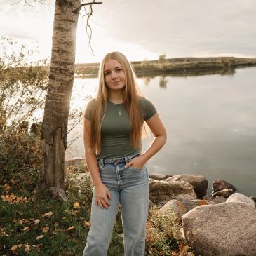 Young woman standing by a lakeside with autumn foliage and rocks.