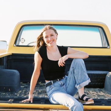 Smiling woman sitting casually on the back of a yellow pickup truck.