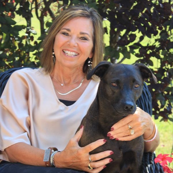 Smiling woman sitting outdoors with her black dog, showing affection.