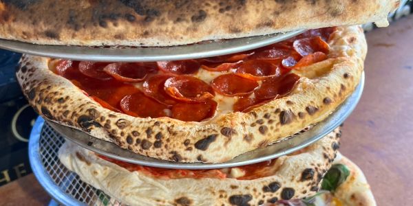 Stacked pizzas with pepperoni and vegetables.